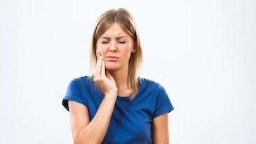 A photo of a woman wincing in pain, holding her cheek with one hand, indicating a toothache